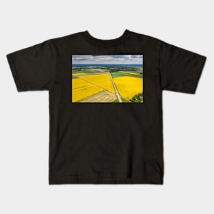 Agricultural landscape, fields of yellow colza and green grain under moody cloudy Kids T-Shirt